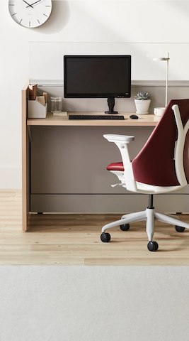 Nurse workstation of Ethospace in an ash veneer with light gray tiles, a monitor and monitor arm, and a Sayl chair in a maroon upholstery and white frame with gray base.