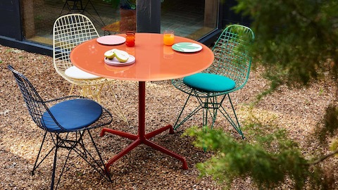 Herman Miller x HAY, outdoor setting of green, black blue, and yellow Wire Chairs and an iron red Eames Table.