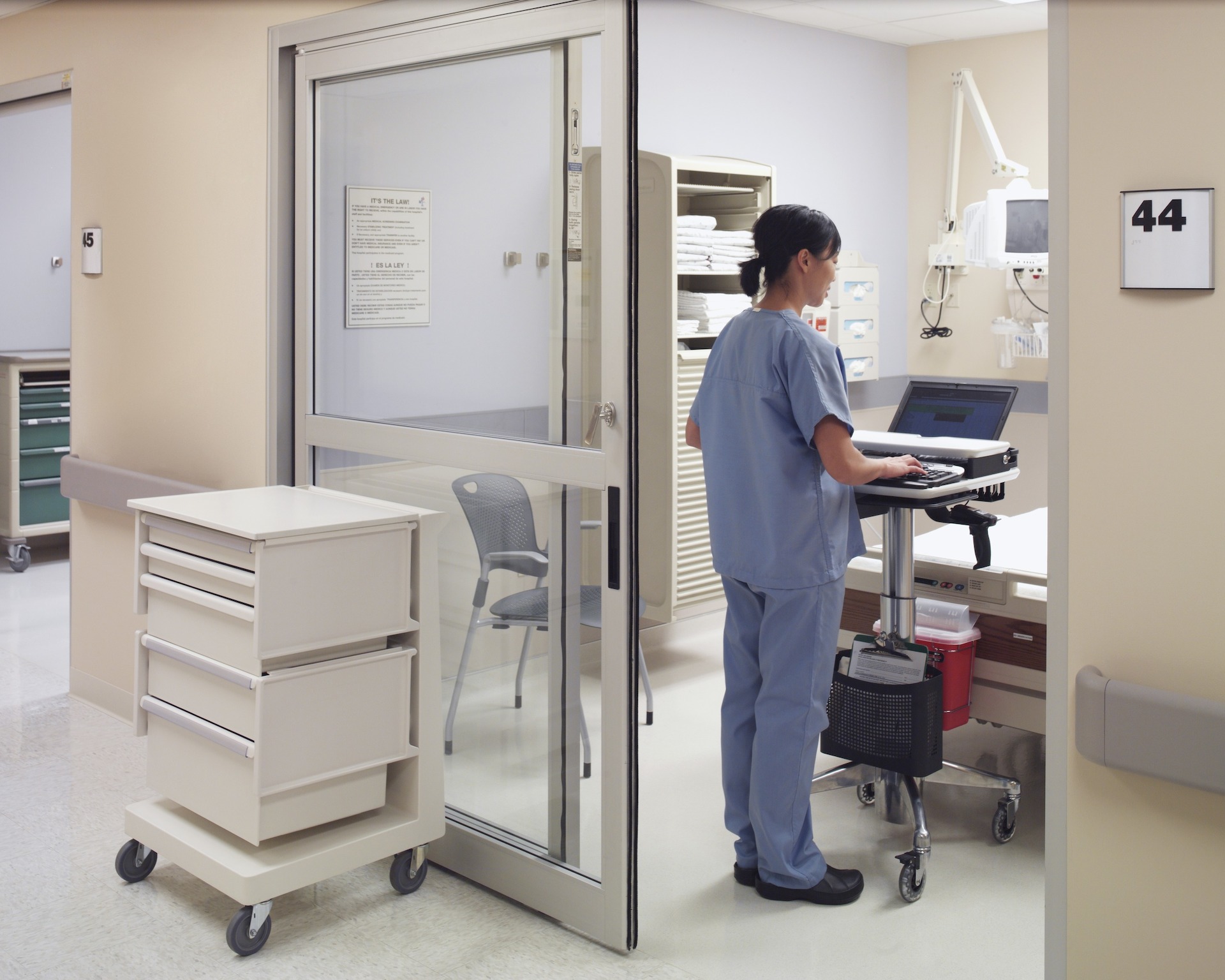 Nurse in blue scrubs working on laptop on Mobile Technology Cart in Emergency Room, Holland Hospital.