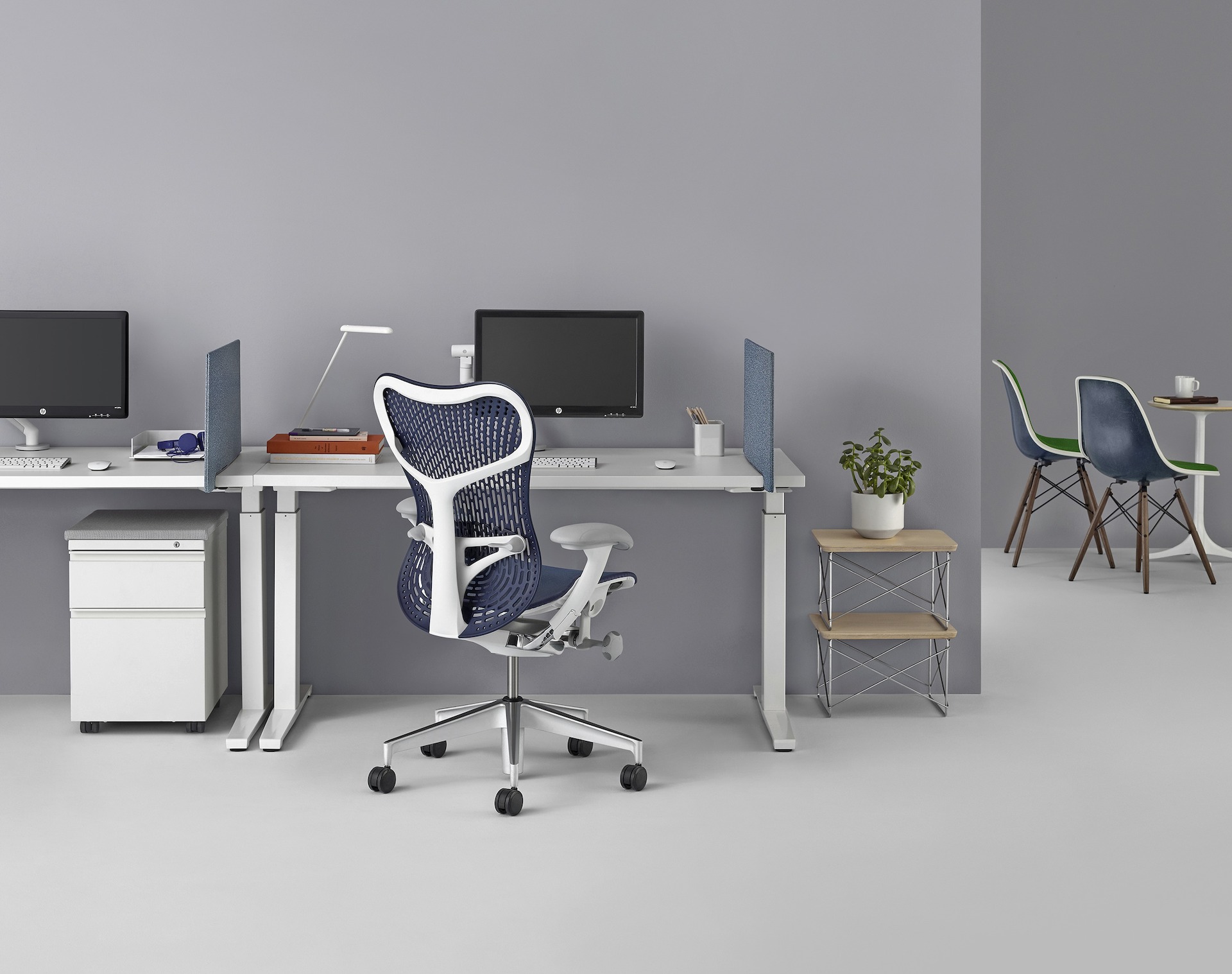 A pair of white Renew Sit-to-Stand tables with blue screens, computer monitors, and a blue Mirra 2 chair.