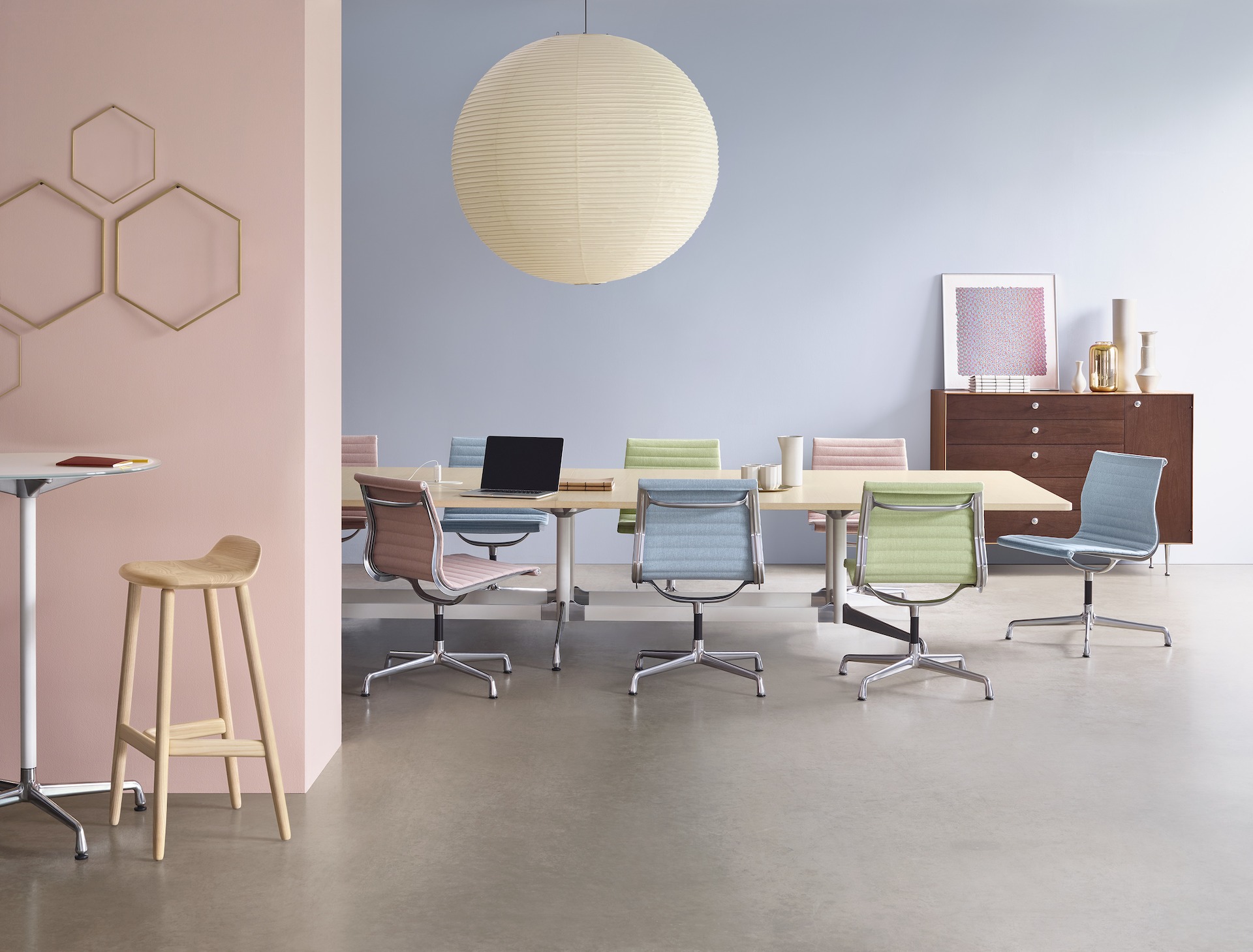 A group of colorful Eames Aluminum Group Side Chairs arranged around a large Eames Table in a Meeting Space.