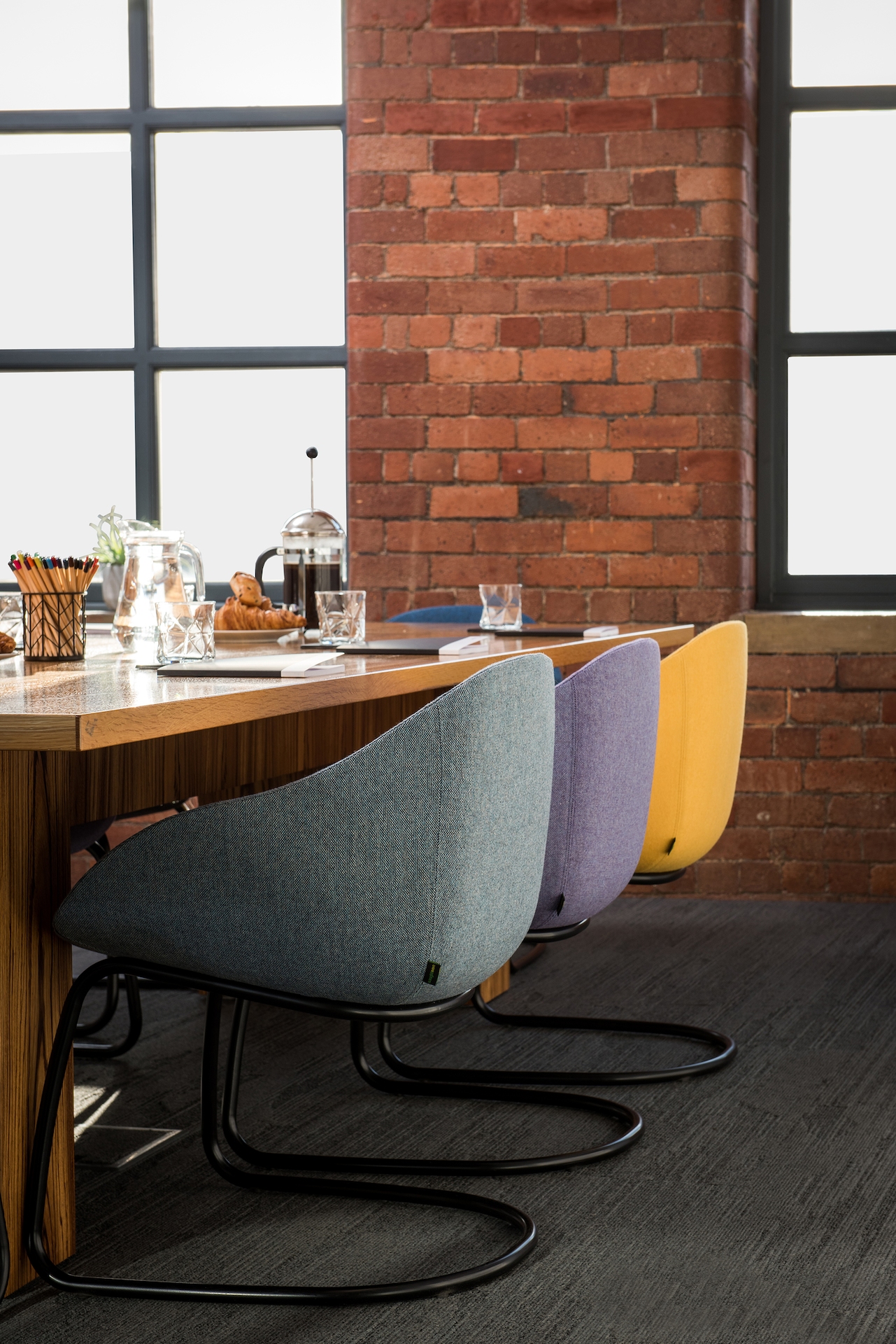 A trio of naughtone Always Side Chairs with black cantilevered bases, upholstered in blue, purple, and yellow, pulled up to a casual cafe bar.