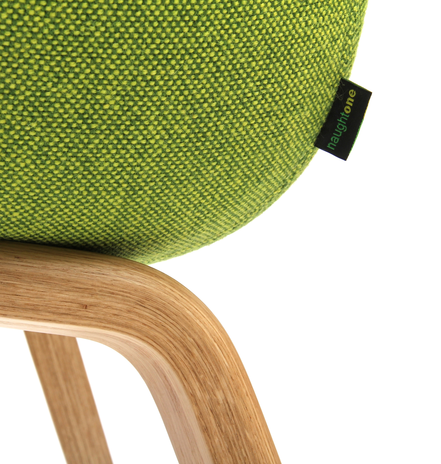 Close-up detail of the naughtone tag on the back left corner of an Always Side Chair, upholstered in textured green fabric and mounted to a wood base.