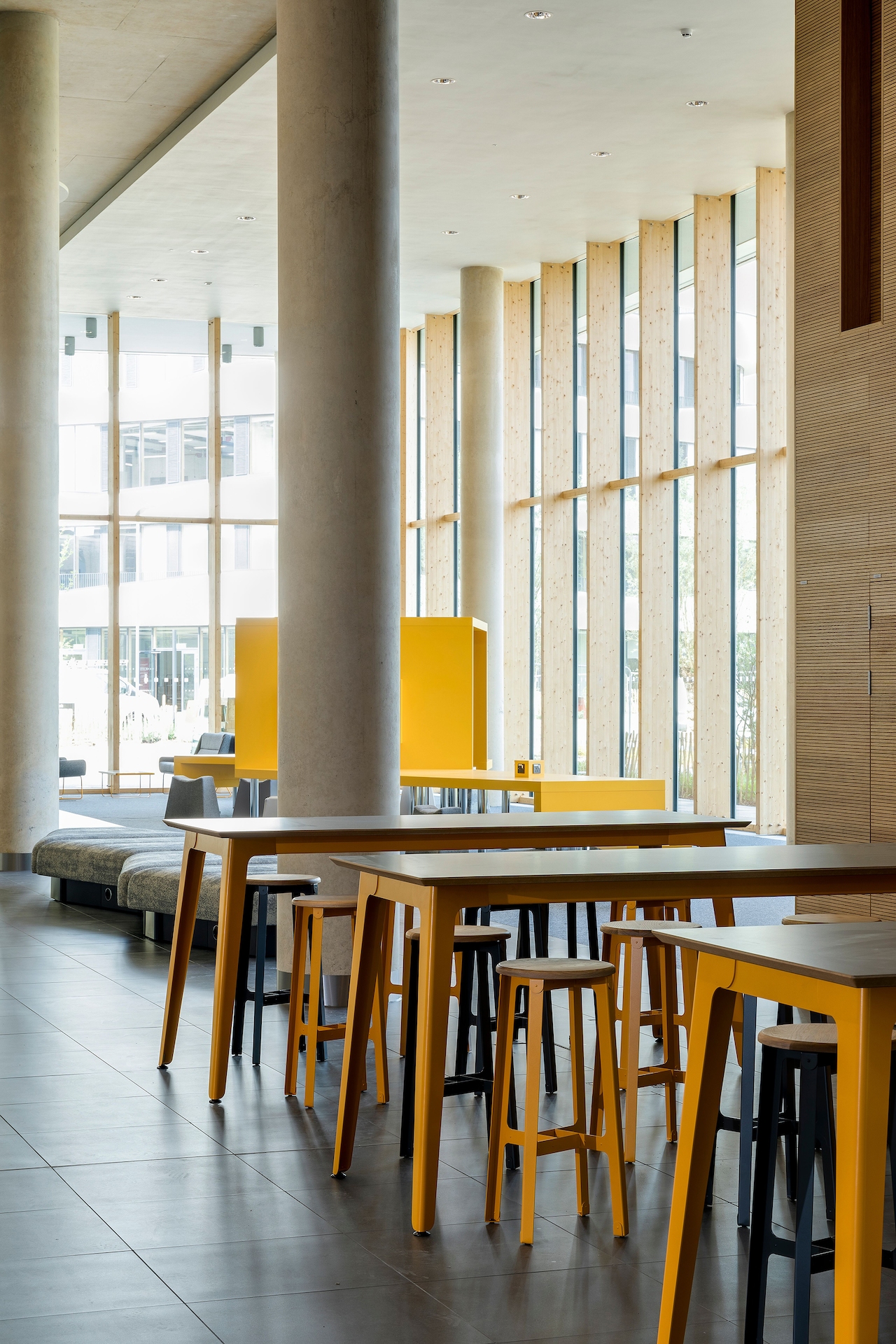 A row of yellow naughtone Fold Bar Height Tables with wood veneer tops, arranged with blue and yellow Construct Stools in a well-lit lobby setting.