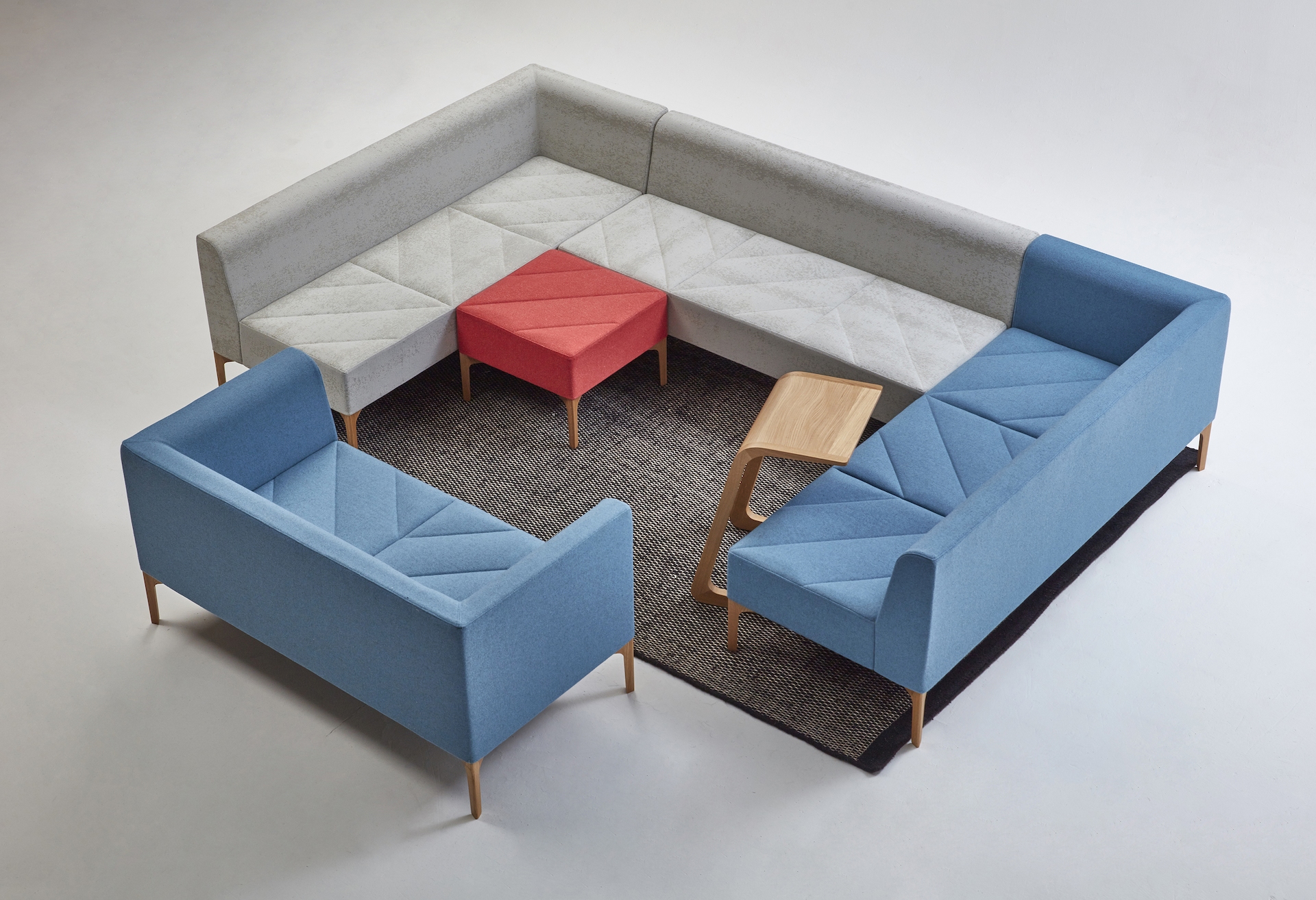 A seating arrangement made of a red Hatch Bench, light blue Sofa, and gray and blue Modular Seating pieces.