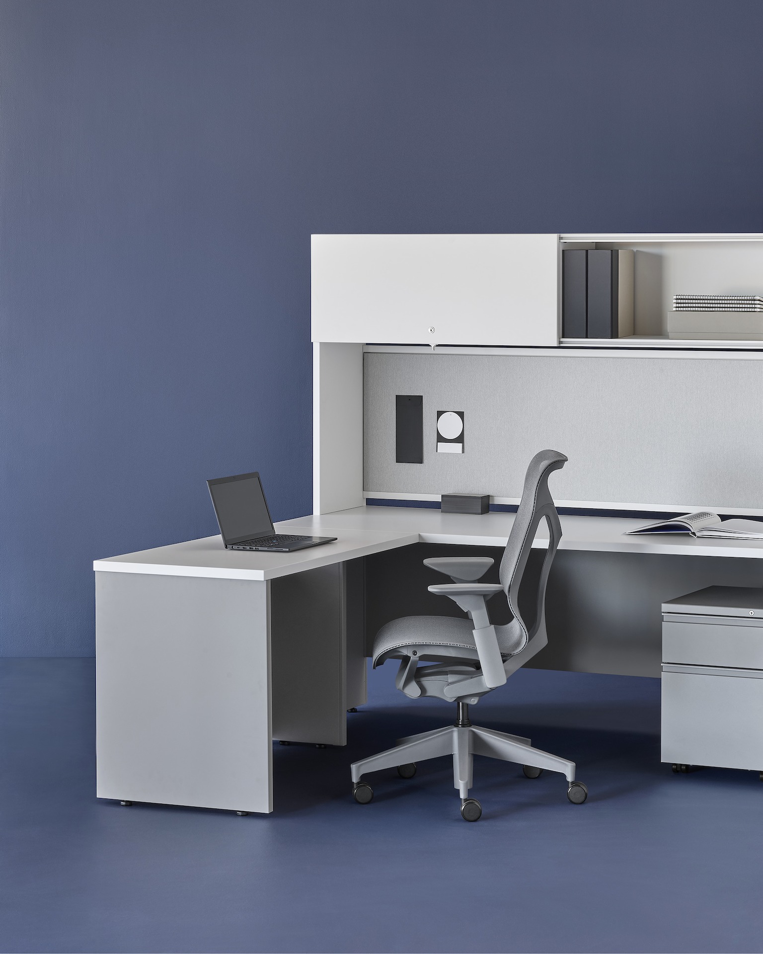 A grey and white Canvas Metal Desk workstation with upper storage, fabric back panel, and grey Cosm Chair.