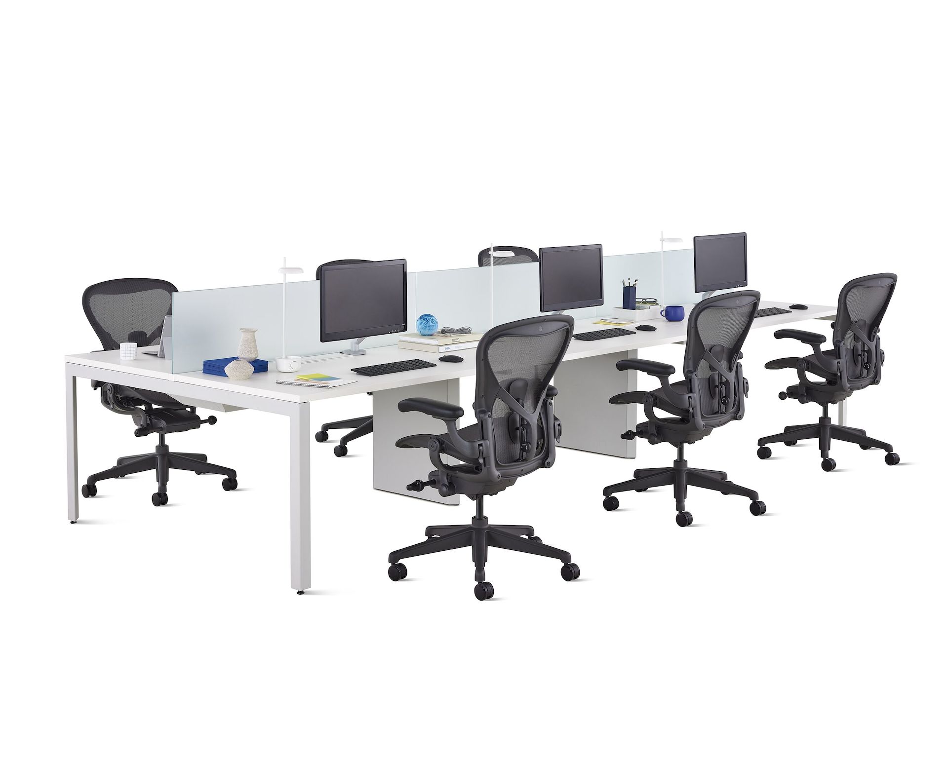 A white Layout Studio benching workstation for six with frosted glass center privacy screens, desk accessories, and six black Aeron Chairs.