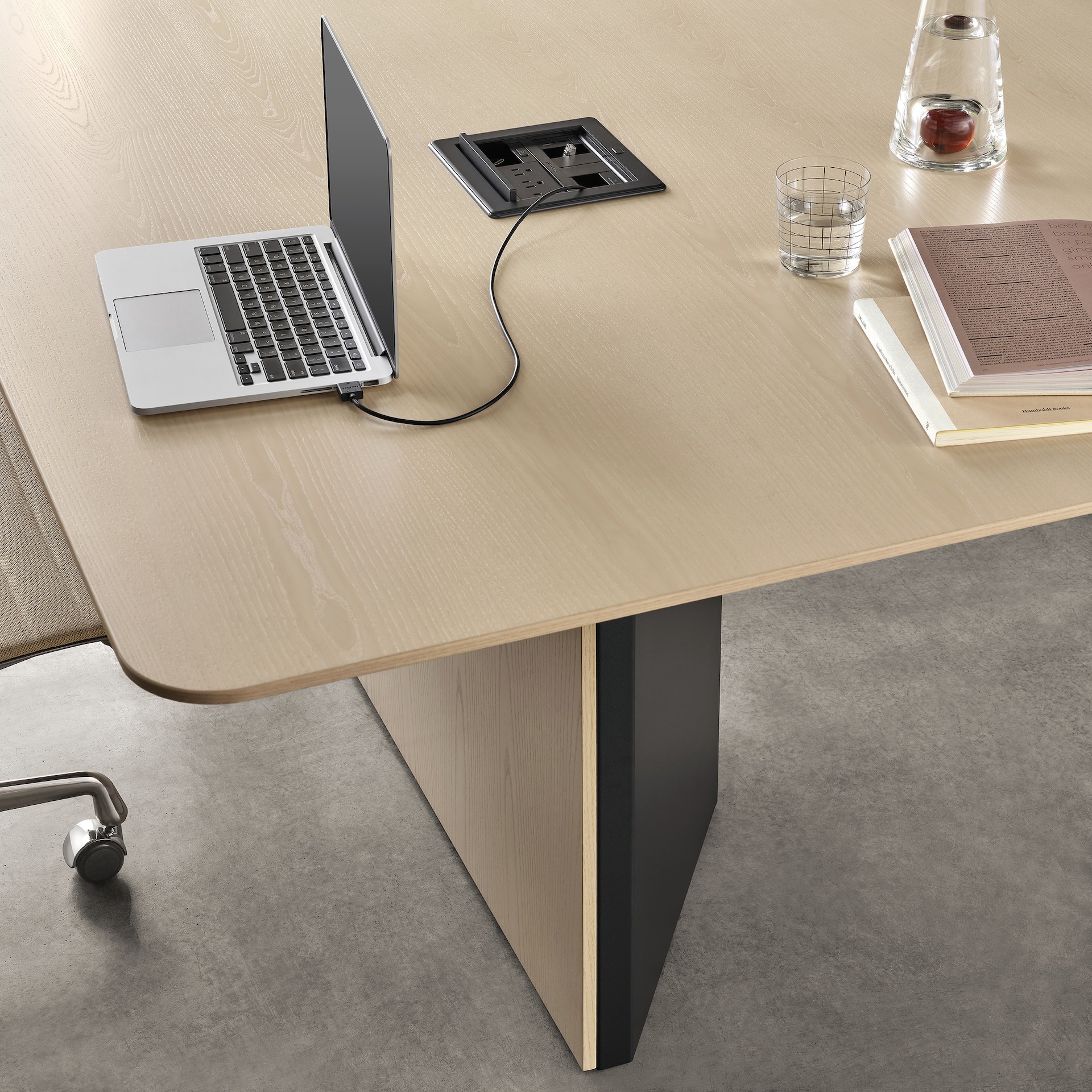 Close-up of a cabinet base Headway conference table, with a laptop on it's surface powered by a tabletop Crestron cord retractor unit.