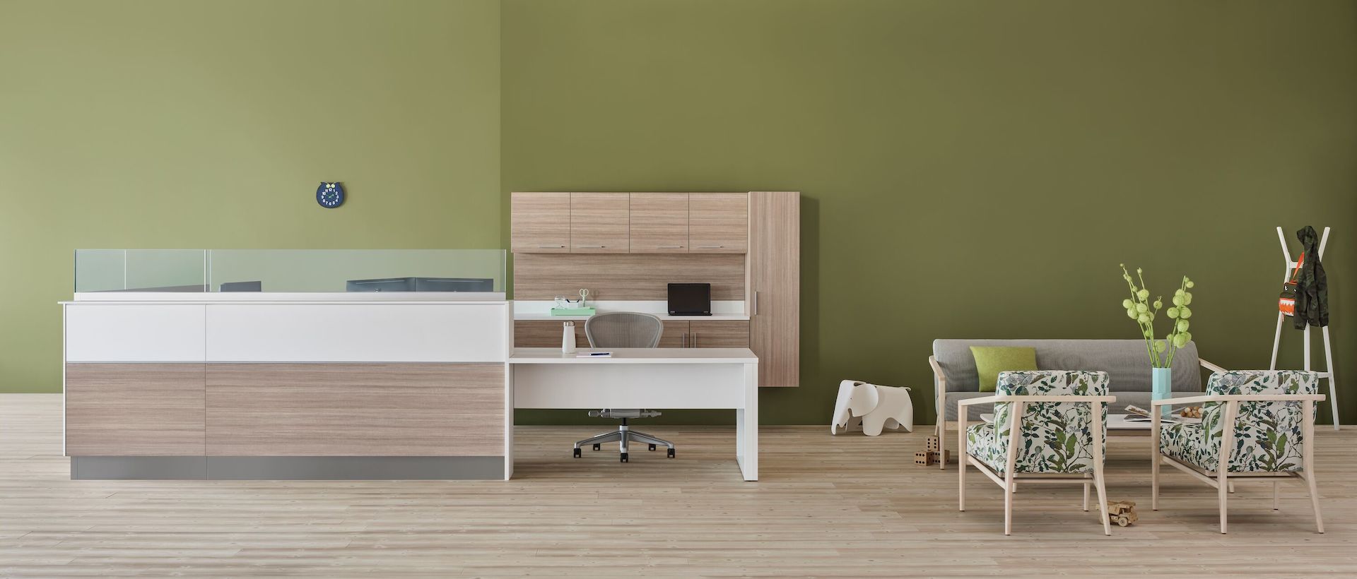 A prefab Commend Nurses Station with glass screens serving as a reception desk in an outpatient space including Palisade chairs, sofa, and table.