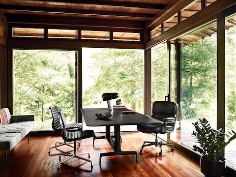 Una mesa AGL negra utilizada como escritorio en una oficina hogareña con paredes de vidrio con vista a los árboles afuera.