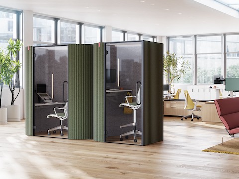 Een zij-aan-zij-weergave van een Bay Work Pod en Bay Work Pod Pro met werkstations op de achtergrond en een loungesetting aan de rechterkant.