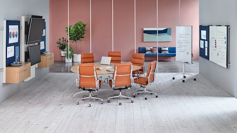 一个泪珠Exclacla会议桌由六个烧焦的橙色Eames Soft Pad椅子包围。