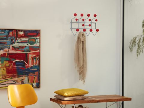An Eames Molded Plywood Chair, Eames Hang-It-All storage rack, and Nelson Platform Bench with metal legs.