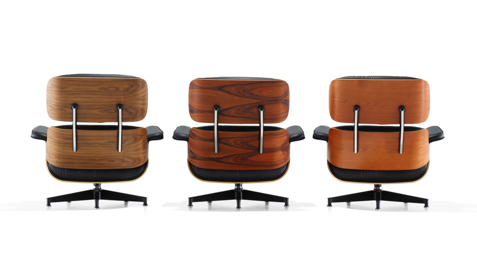 Three Eames Lounge Chairs, each with a different wood veneer finish, viewed from the rear. 