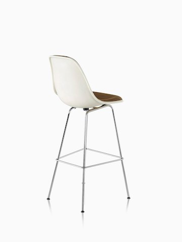 一个白色的Eames模制玻璃钢凳子与棕色室内装潢的四分之三后视图。