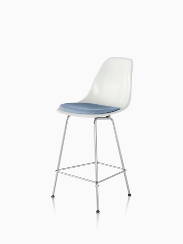 白色Eames模塑玻璃纤维凳子，从45度角看，带浅蓝色座垫。