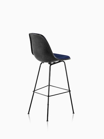 黑色Eames模压玻璃钢凳子与蓝色室内装潢的四分之三后视图。