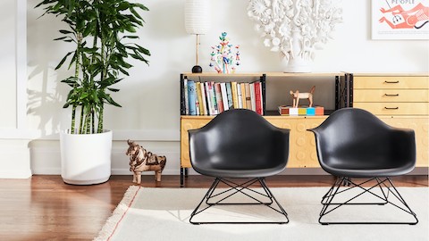 Two Eames Moulded Plastic Armchairs with low wire bases on a rug in a living room setting.