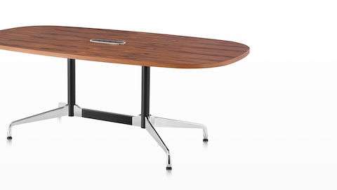 An oval Eames meeting table with a medium wood finish and a central cutout for cord access.