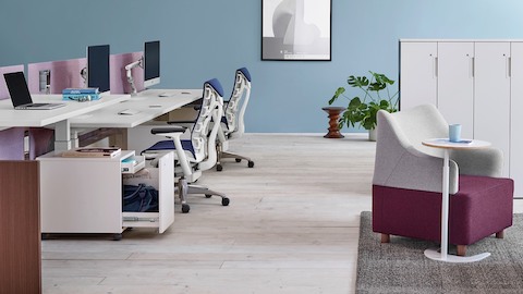蓝Embody办公椅和白色Renew链接高度可调的工作表面，在一个长椅上工作。