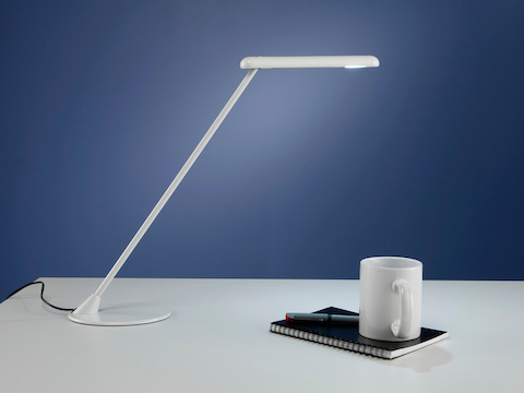 A white freestanding Flute Personal Light joins a notepad and coffee cup on a desktop.