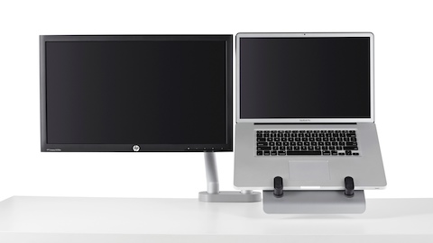 A dual monitor arm lifts both a computer screen and notebook computer, using a laptop mount, off the work surface.