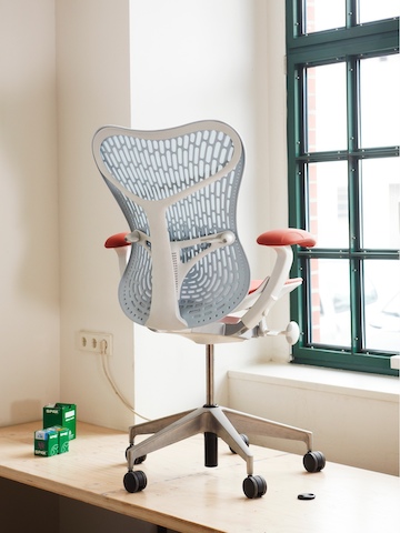 A blue Mirra 2 office chair, viewed from the rear and set close to a window.