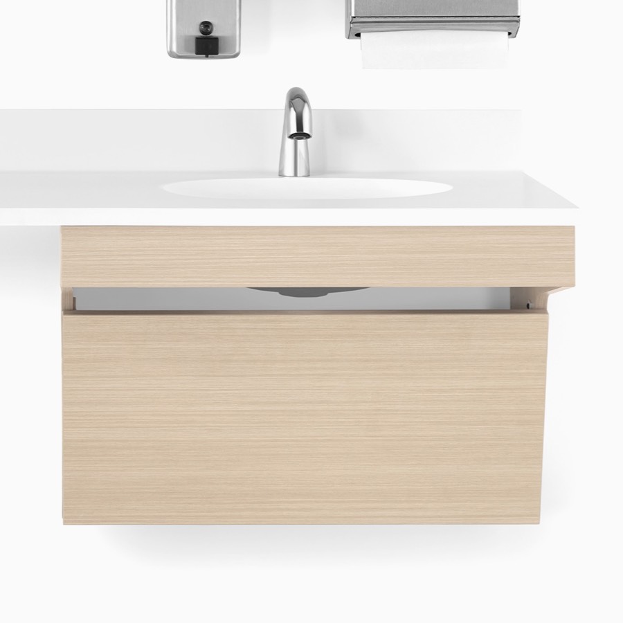 A close-up view of a Mora Systems casework ADA sink enclosure in an ash finish with a white solid surface top and ADA sink.