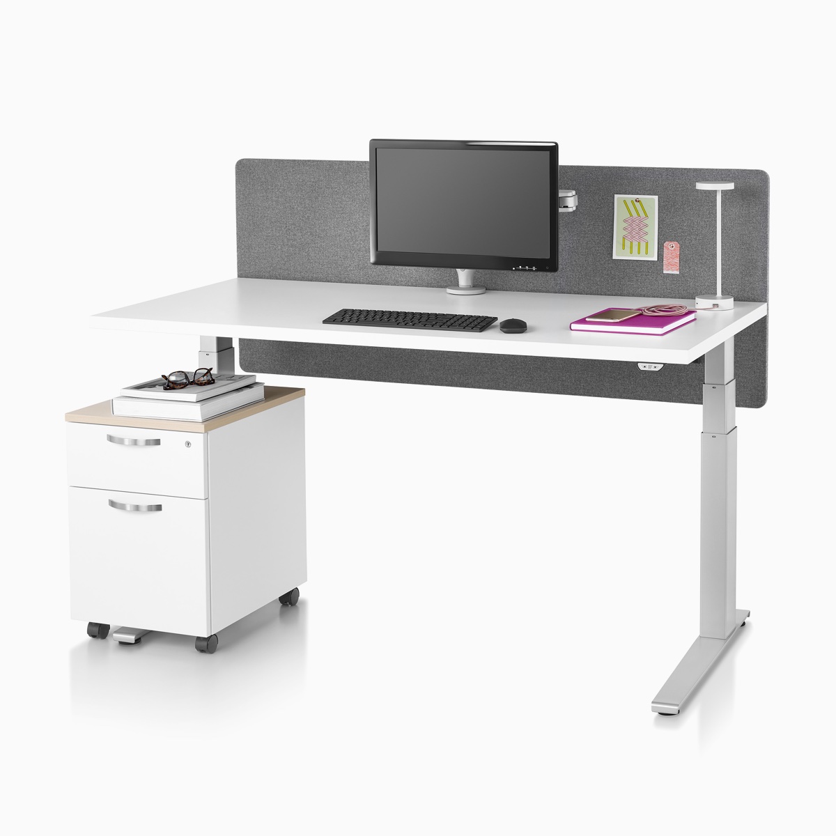 A Motia standing desk with a white top, metallic silver base, surface-attached privacy screen, desk lamp, and a Tu Wood pedestal.
