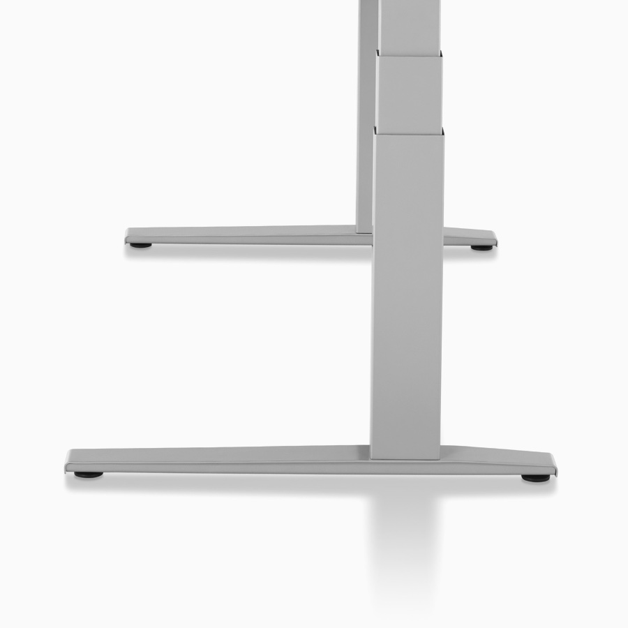 Side profile of a Motia Sit-to-Stand Table, with a white work surface and metallic silver C-leg base at a seated height.
