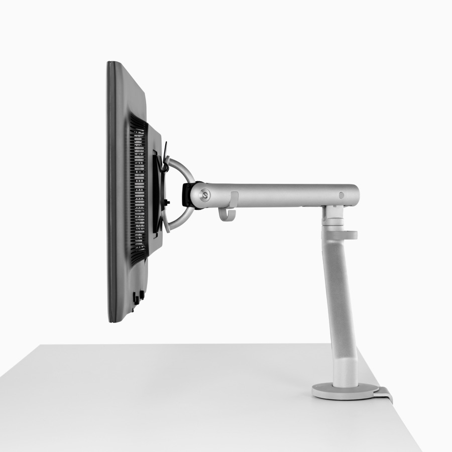 Side profile of a silver single Flo Monitor Arm holding a screen and attached to a white work surface.