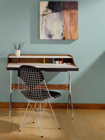 Un espacio de trabajo residencial equipado con un escritorio Nel Swag Leg y una silla de alambre Eames con un parche de bikini negro.