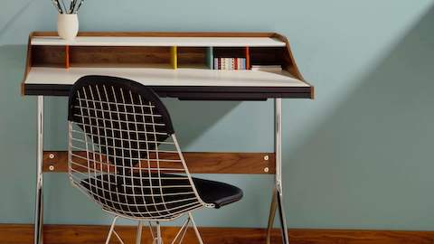 A residential workspace outfitted with an Nelson Swag Leg Desk and an Eames Wire Chair with a black bikini pad.
