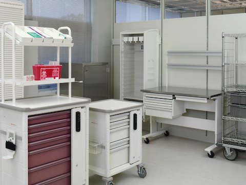 Uma sala de serviços de saúde que contém vários carrinhos de procedimento / suprimentos com gavetas e acessórios intercambiáveis.