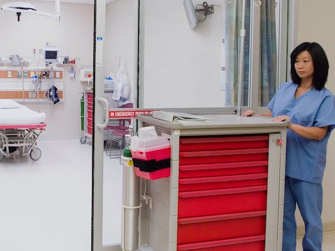 Uma enfermeira empurra um Carrinho de Suprimento / Procedimento móvel com sete gavetas intercambiáveis.