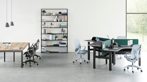 An open office environment with a cluster of 3 Ratio 120 desks positioned at varying heights to the right and a large Layout table on the left. A selection of high and low back Cosm chairs are positioned around the desks with a bookcase in the background.