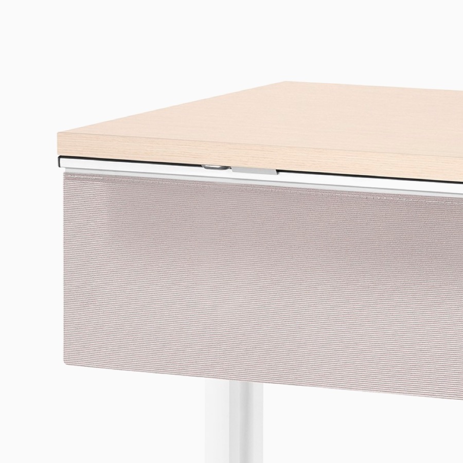 Viewed at an angle, a rectangular Everywhere Table with clear on ash woodgrain laminate work surface, white base, and a fabric modesty panel.