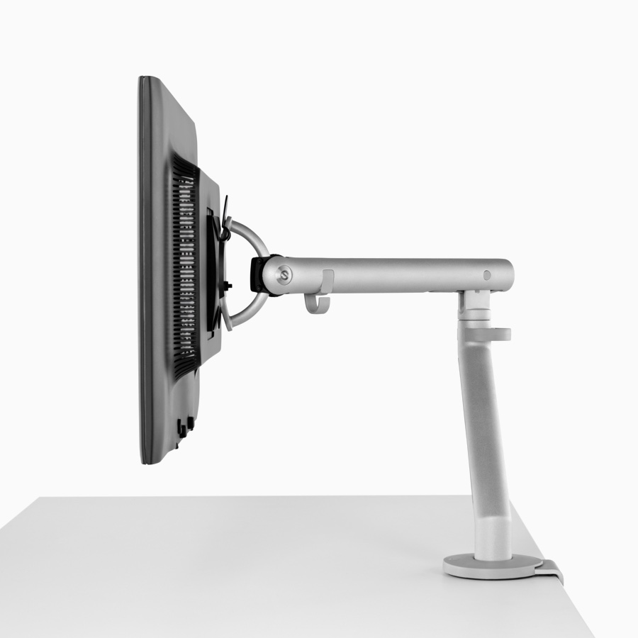 Side profile of a silver, single Flo Monitor Arm holding a screen and attached to a white work surface.