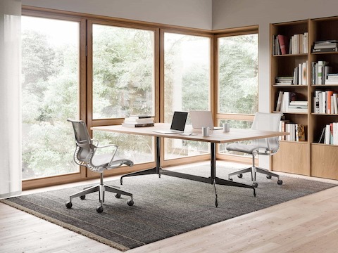 Two Setu Chairs in light grey on opposite sides of a rectangular table in a home office with a bookshelf.