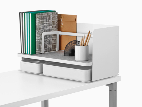 Ein großer, weißer Ubi-Desktop-Organizer mit einem grauen, rutschfesten Regal enthält Bücher, einen Stiftbecher und zwei Aufbewahrungsboxen.