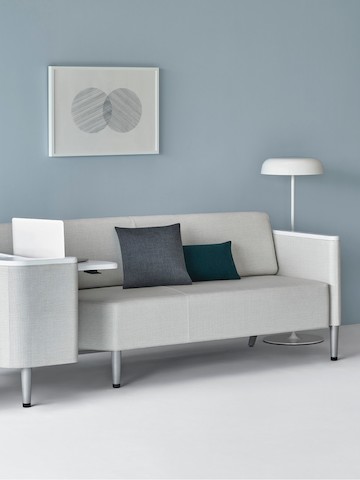 A Palisade Flop Sofa in light gray textile with white solid surface arm caps and white adjustable table with Durawrap top.