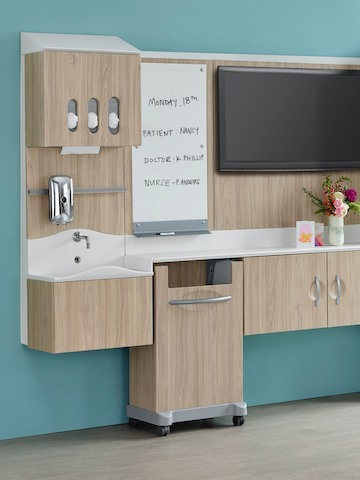 A patient room environment with a Compass System footwall in a light wood finish.