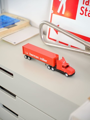 A toy truck with Herman Miller's signature red and logo sits atop a gray filing cabinet. 