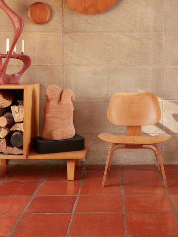 An Eames Molded Plywood Lounge Chair with a wood base next to a scuplture.