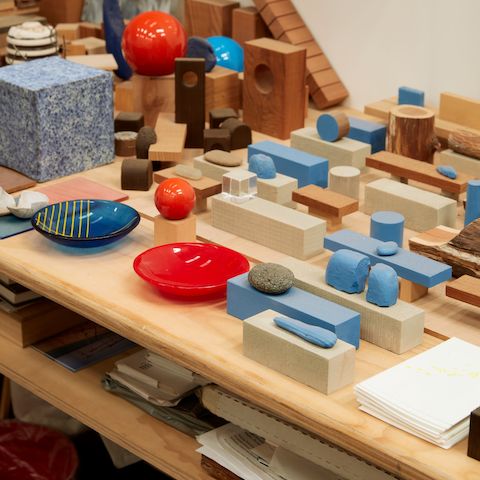 Small models of Jesse Schlesinger's works in progress alongside red and blue glass dishes.