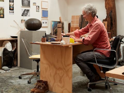 Jesse Schlesinger seated on a black Eames Soft Pad Chair in his woodworking studio.