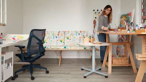 Artist Kindah Khalidy painting in her studio, standing with a Cosm Chair and a Passport Table.