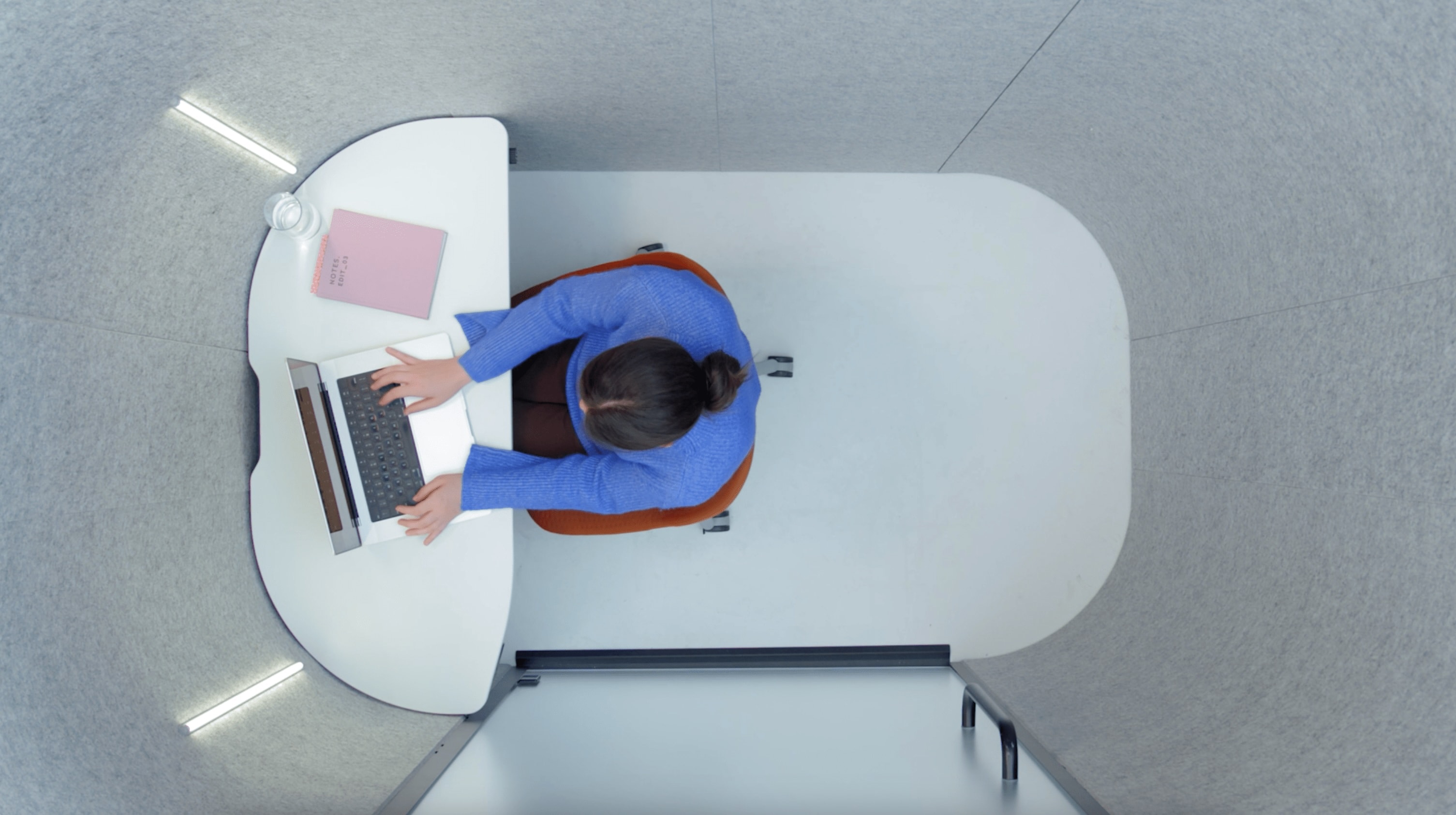 Overhead view inside the Bay Work Pod showing a woman working on a laptop.