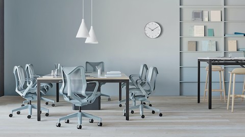 Verschillende Cosm-stoelen met lage rugleuning in lichtblauwe afwerking staan rond een Layout Studio-vergadertafel in een luchtige open kantoorruimte. Selecteren om een Herman Miller dealer te zoeken.
